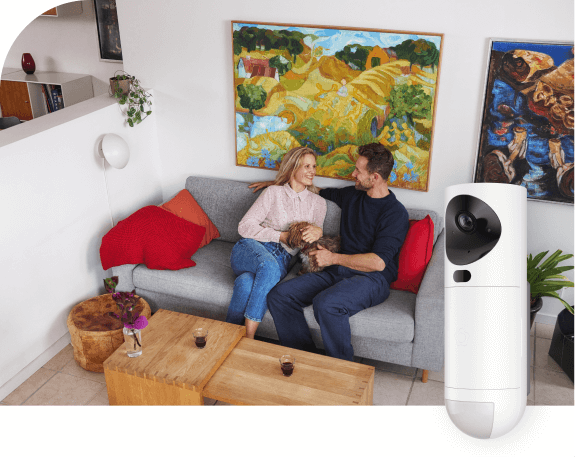 GuardVision-kamerailmaisin sisävalvontaan. Pariskunta istuu olohuoneen sohvalla hymyillen ja pientä koiraa pidellen.